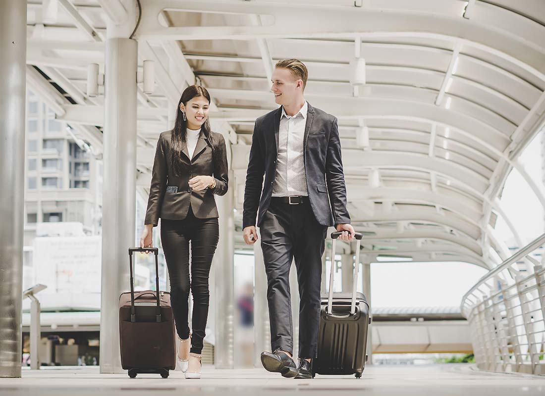International Business Insurance - Business Man and Woman Going on an International Business Trip Walking Away From the Camera and Pulling Luggage in an Airport Terminal