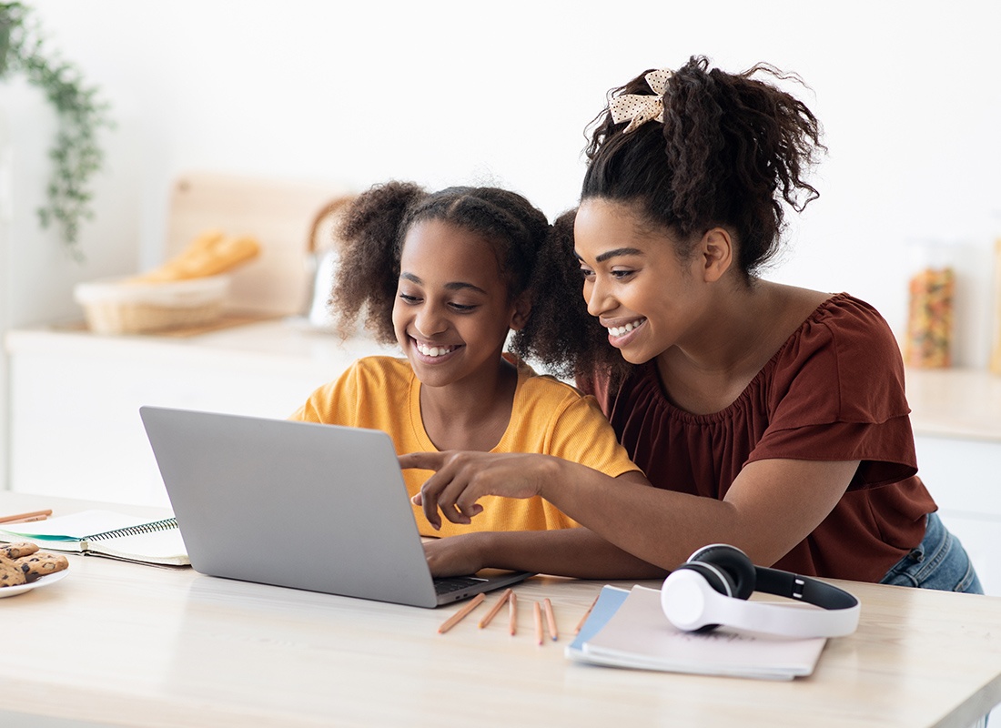 Insurance Solutions - Happy Mother and Daughter Sit Together Using a Laptop at Home